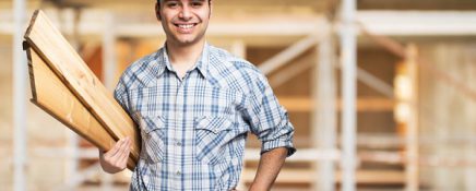 Portrait of a smiling carpenter holding wood planks in a construction site