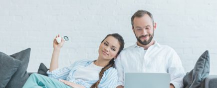 couple turning on air conditioner during the summer heat while using laptop