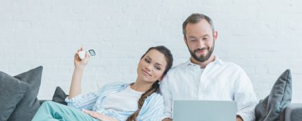 couple turning on air conditioner during the summer heat while using laptop