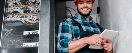 happy bearded technician in safety helmet holding digital tablet