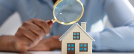 Businesswoman Holding Magnifying Glass Over House Model