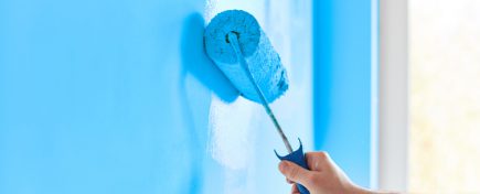 Male hand painting wall with paint roller. Painting apartment, renovating with blue color paint