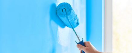 Male hand painting wall with paint roller. Painting apartment, renovating with blue color paint