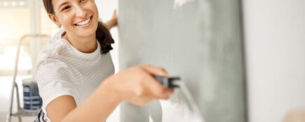 Young woman painting a wall at home after Home Renovation Technician Training.