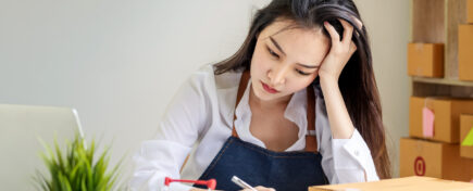 Female supply chain professional sitting at desk with laptop, notebook, and shipping boxes
