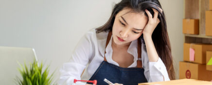 Female supply chain professional sitting at desk with laptop, notebook, and shipping boxes